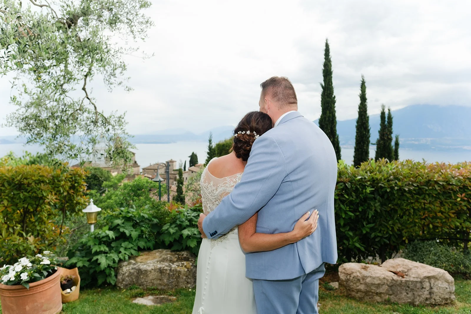 Sposi abbracciati di spalle, affacciati sul Lago di Garda fra gli ulivi Sposi abbracciati di spalle, affacciati sul Lago di Garda fra gli ulivi